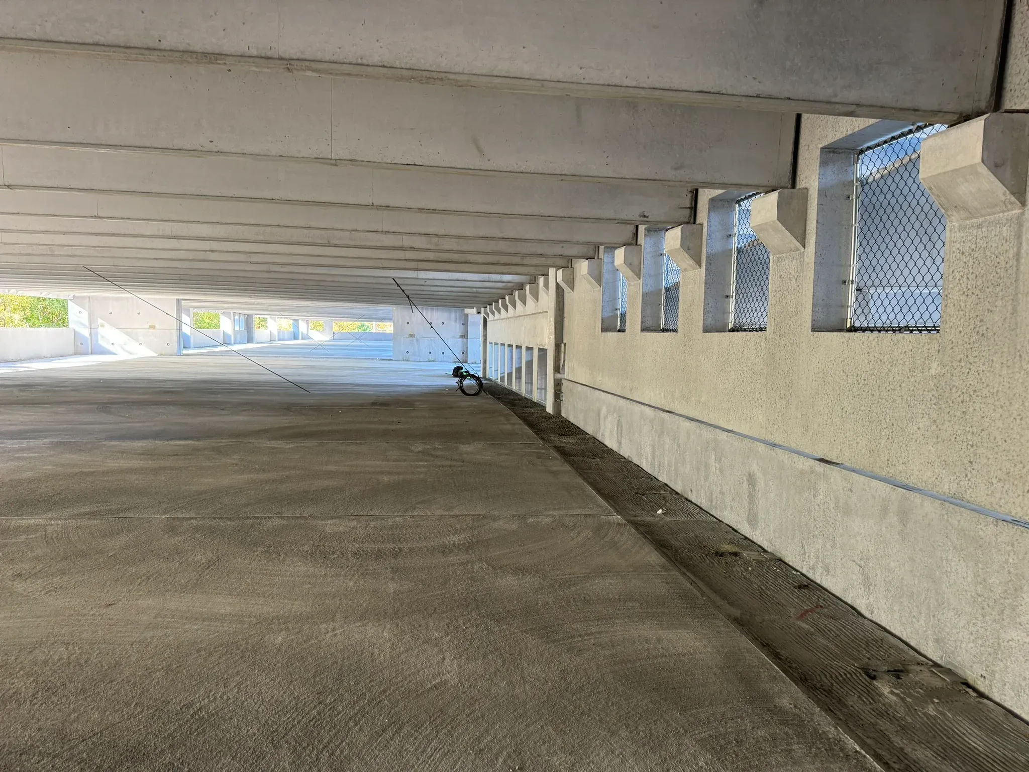 Interior view of an unfinished concrete parking garage level with open perimeter wall sections, chain-link safety screening, and a smooth newly finished floor.